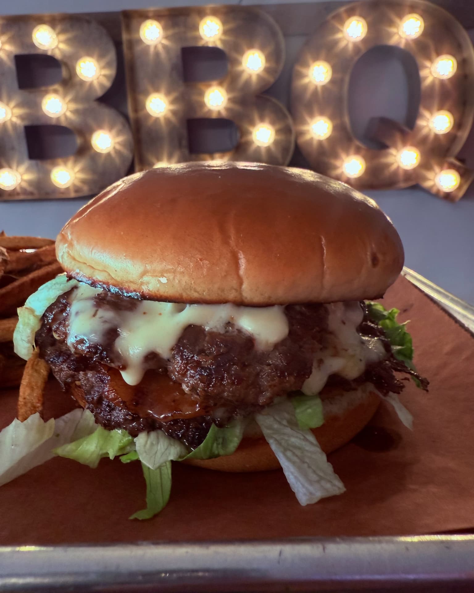 Sauced cheeseburger with lettuce beneath the BBQ marquee