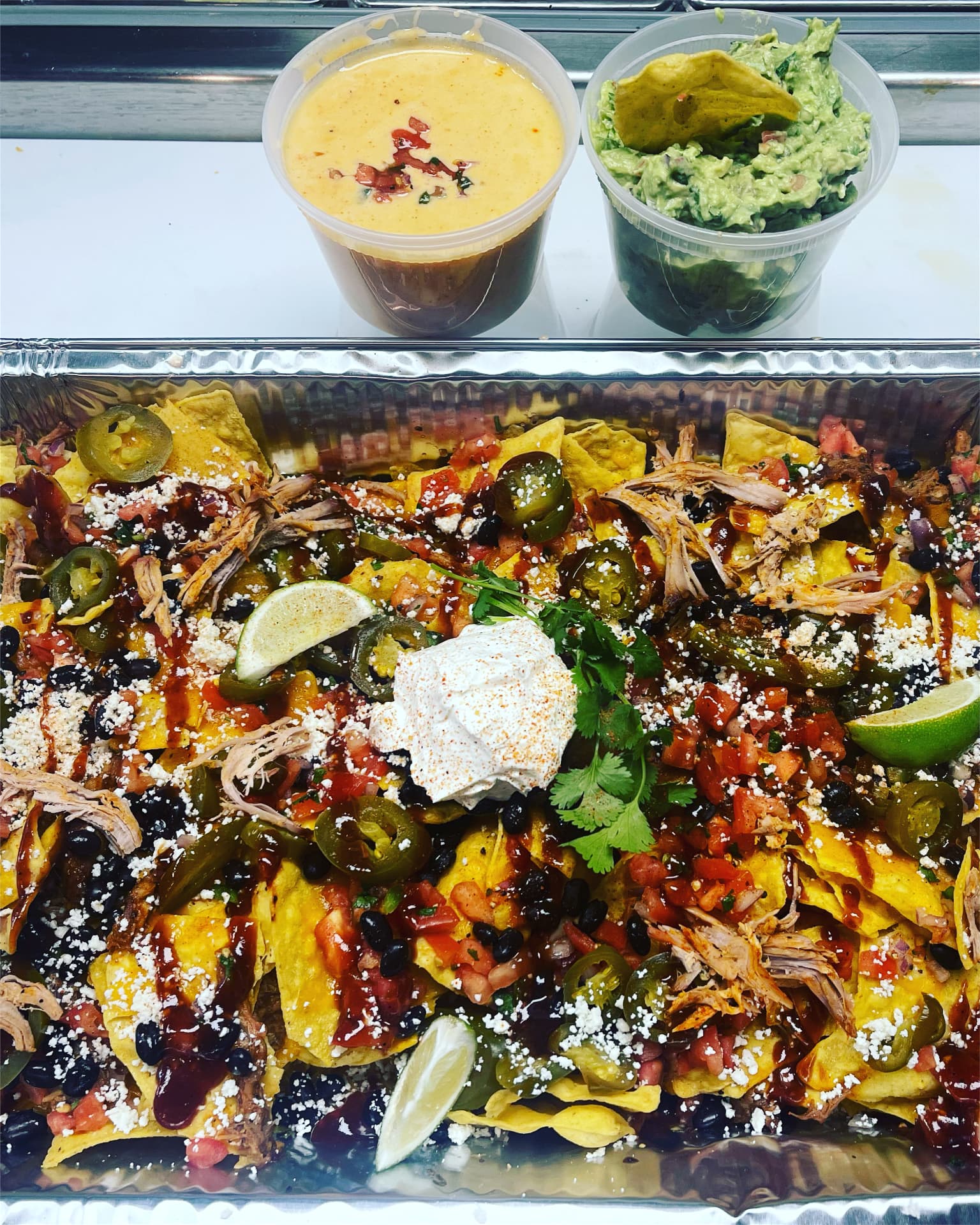 Catering tray of loaded barbecue nachos with queso and guacamole